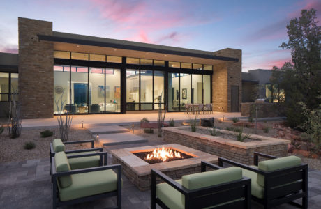 Modern house with large windows and outdoor fire pit at twilight.