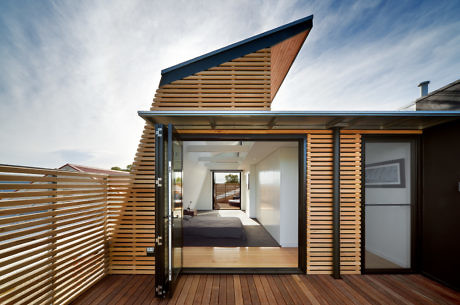 Modern bedroom extension with wooden slats and deck, angled roof, and sliding glass
