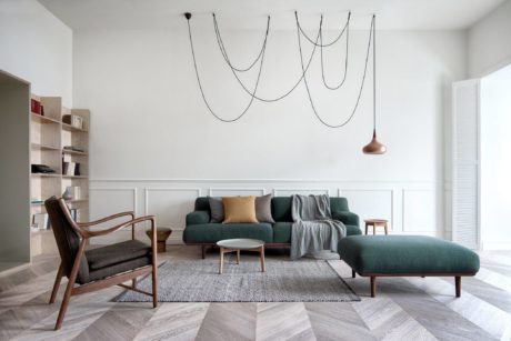 Modern living room with green sofa, wooden chair, and unique wall art.