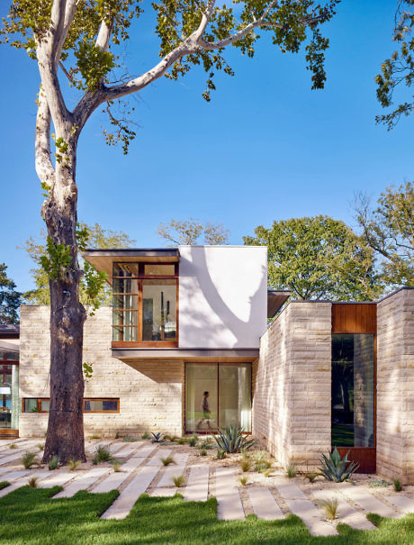 Modern two-story house with large windows, stone facade, and landscaped garden.