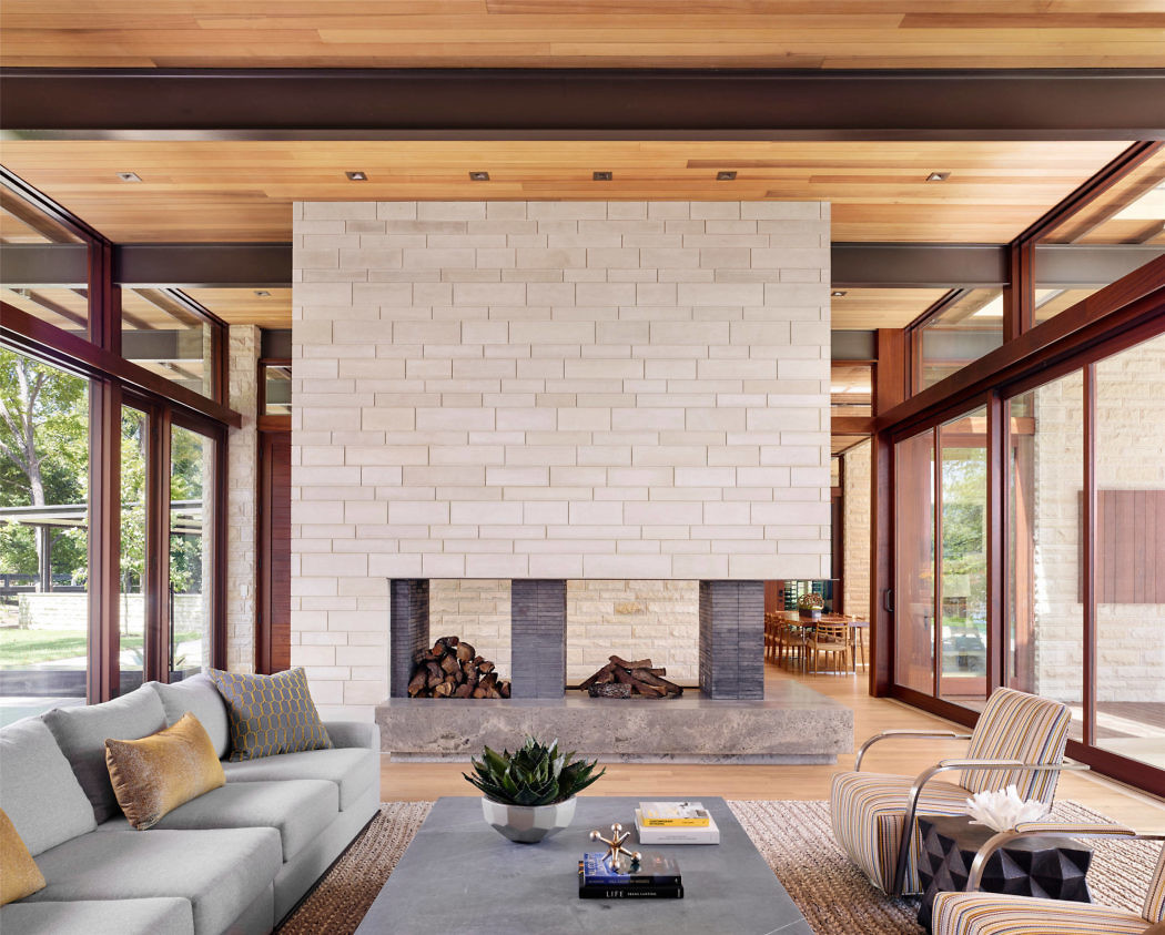 Modern living room with a large white fireplace, wooden ceiling, and glass walls.