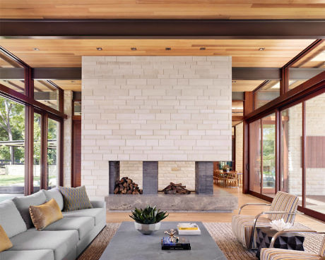 Modern living room with a large white fireplace, wooden ceiling, and glass walls.