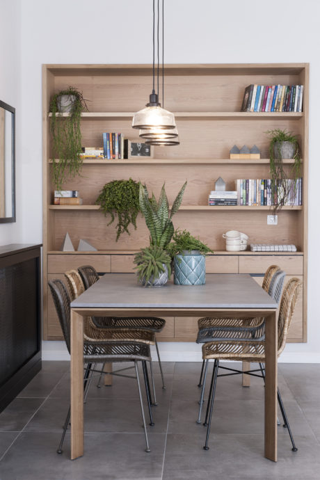 Modern dining area with wooden shelving, plants, and pendant light.