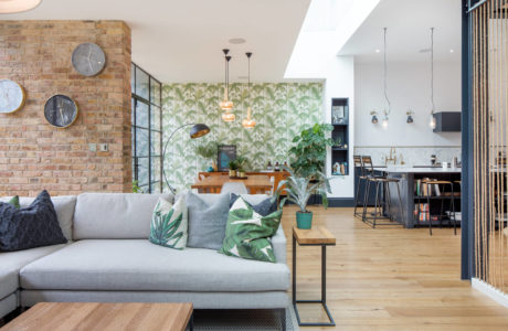 Modern living room with exposed brick, patterned wallpaper, and open-plan kitchen.