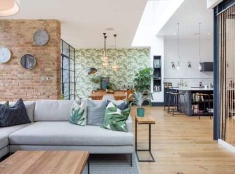 Modern living room with exposed brick, patterned wallpaper, and open-plan kitchen.