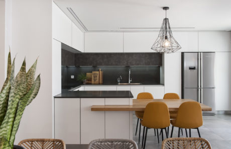 Modern kitchen with white cabinets, black backsplash, wooden table, and brown chairs