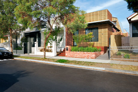 Modern house with wooden slats next to traditional homes on a street.