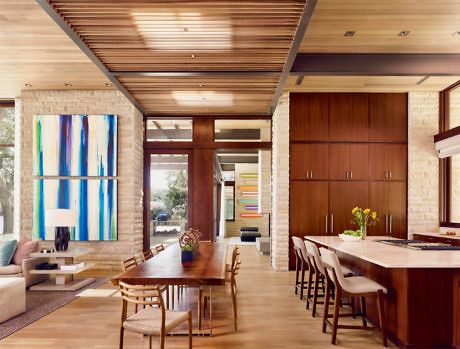 Modern living room with dining area, wooden ceiling, and colorful art.