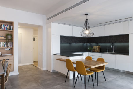 Contemporary kitchen with geometric light fixture, black backsplash, and yellow chairs.