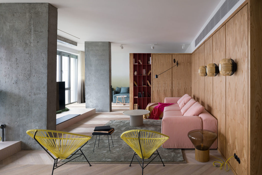 Modern living room with pink sofa, yellow chairs, and wooden paneling.