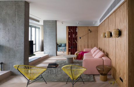 Modern living room with pink sofa, yellow chairs, and wooden paneling.