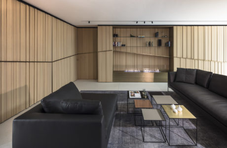Modern living room with wooden panel walls, black sofas, and geometric coffee tables.