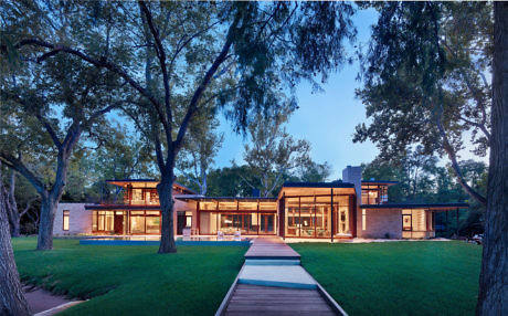 Contemporary home with expansive glass walls amidst lush trees.