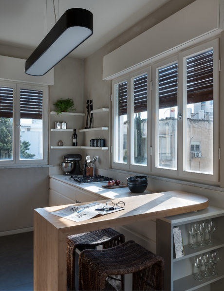 Modern kitchen with wooden countertop, bar stools, and large windows with blinds.
