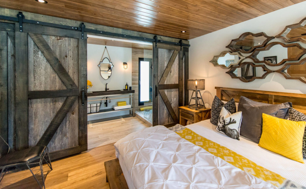 Rustic bedroom with sliding barn door, wooden ceiling, and decorative mirror.