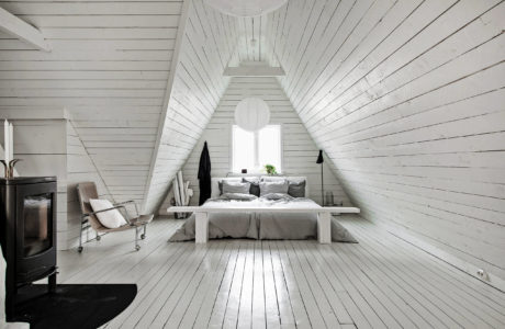 Minimalist attic bedroom with white plank walls and floors, fireplace, and circular window