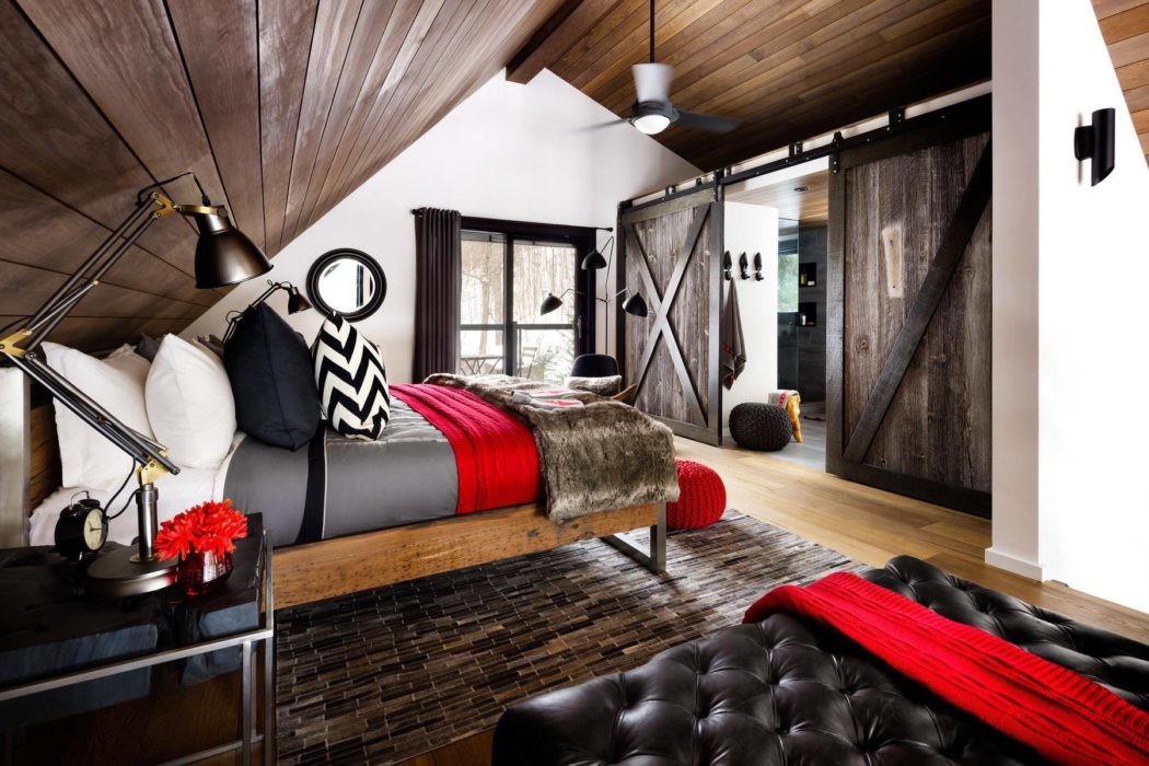 Modern bedroom with wooden ceiling, barn door, and black leather sofa.