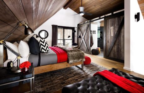 Modern bedroom with wooden ceiling, barn door, and black leather sofa.