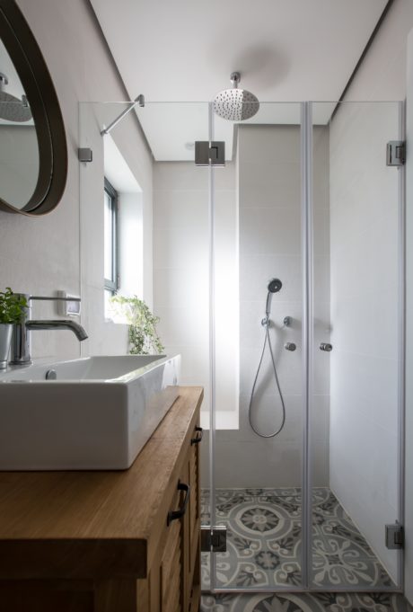 Contemporary bathroom with patterned floor tiles, glass shower, and wooden vanity.