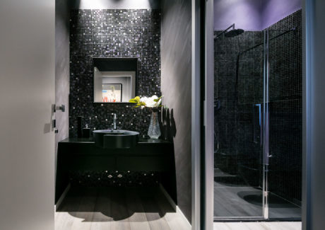 Modern bathroom with black mosaic tiles and glass shower door.