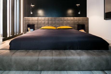 Contemporary bedroom with a large gray bed and contrasting yellow pillows.