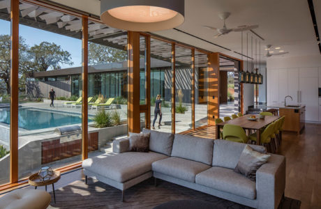 Modern living room with large windows overlooking a pool and a person walking outside.