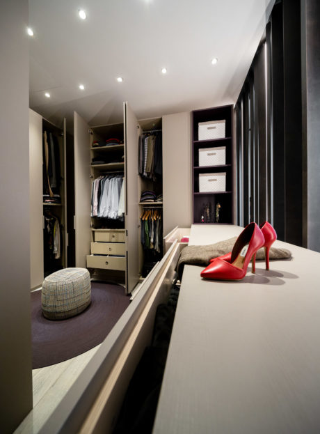 Modern walk-in closet with red high heels on a bench.