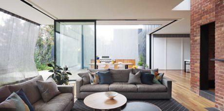Modern living room with large windows, sectional sofa, and exposed brick wall.