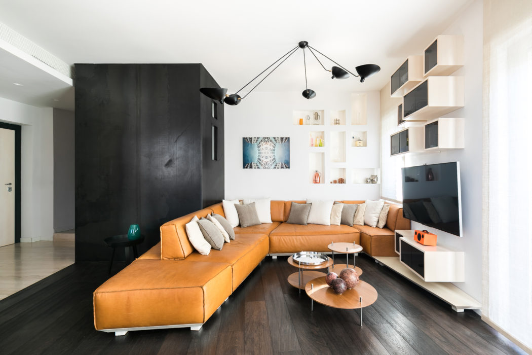 Contemporary living room with L-shaped orange sofa and sleek black wall unit.