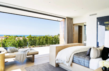 Modern bedroom with open sliding door to seaside view.