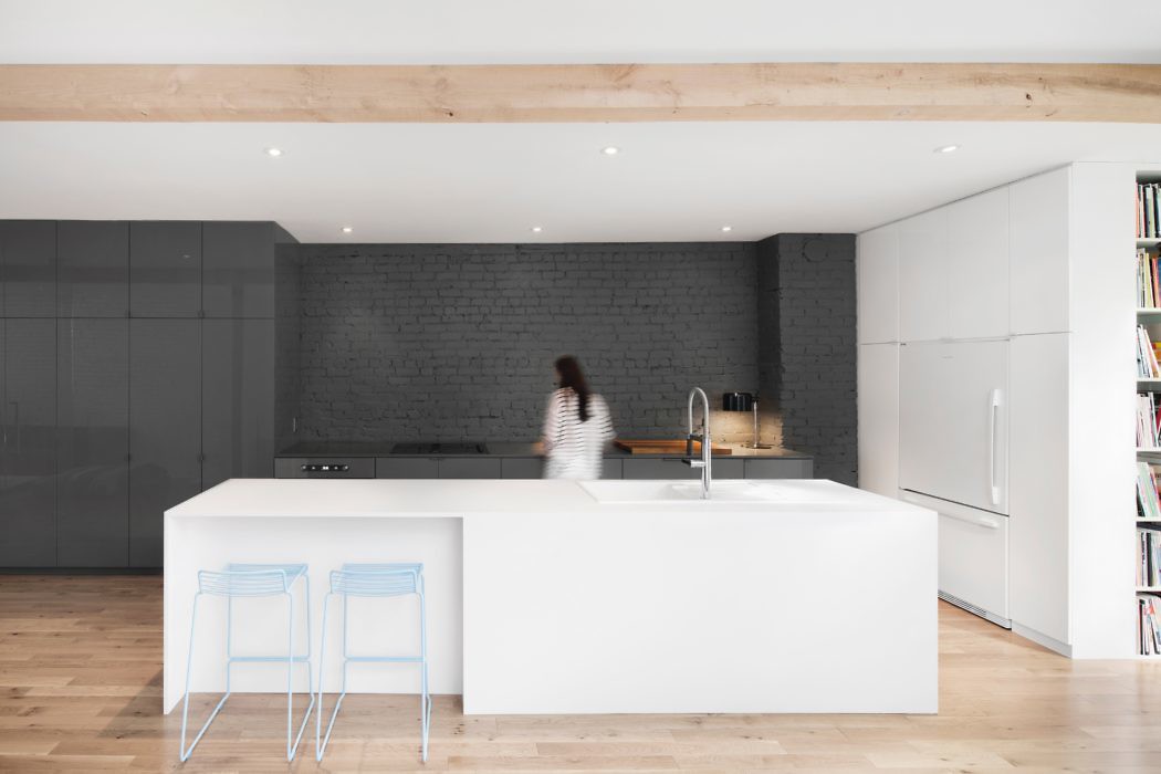 Minimalist kitchen with white island, wooden floors, and grey backsplash.