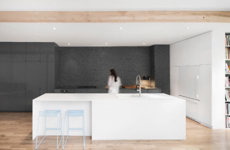 Minimalist kitchen with white island, wooden floors, and grey backsplash.