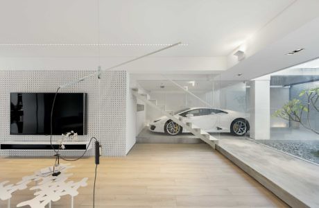 Modern living room interior with visible parked car through glass wall.