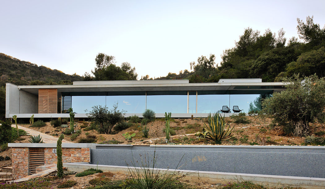 Sleek glass-walled house with flat roof, nestled in a hilly