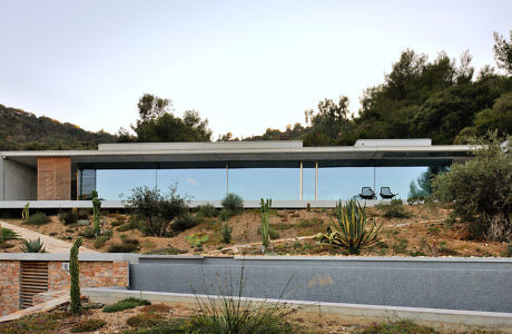 Sleek glass-walled house with flat roof, nestled in a hilly