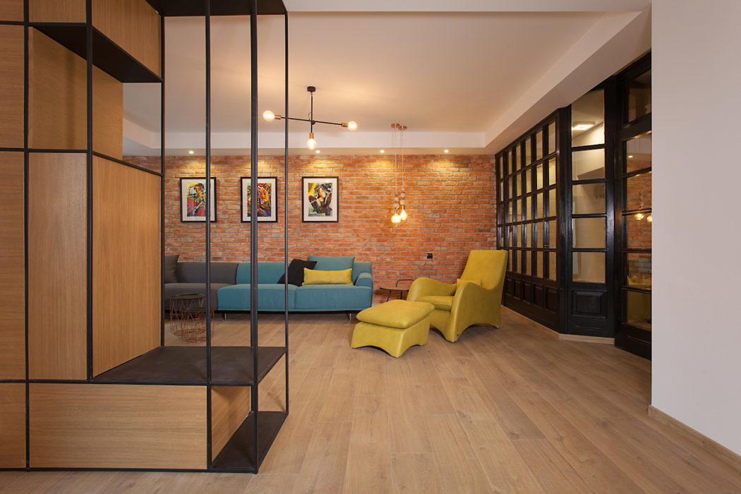 Modern room with brick wall, teal sofa, yellow chairs, and wooden floors.