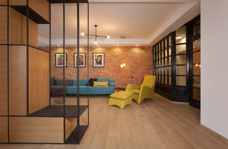 Modern room with brick wall, teal sofa, yellow chairs, and wooden floors.