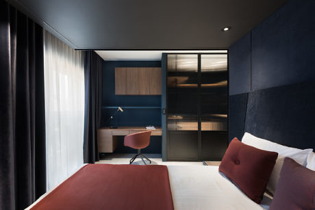 Contemporary bedroom with blue accents, sleek furniture, and glass closet doors.