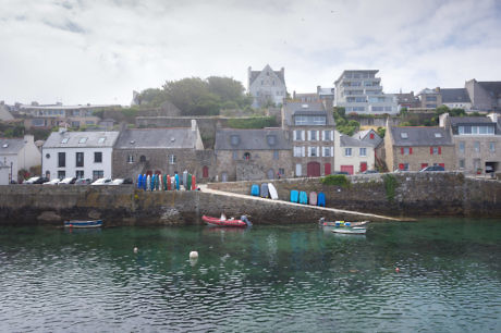 Coastal town with stone buildings, boats, and a small harbor under a