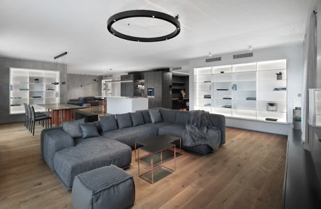 Modern living room with gray sectional sofa, wooden floor, and white shelves.