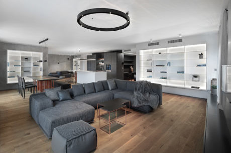 Modern living room with gray sectional sofa, wooden floor, and white shelves.