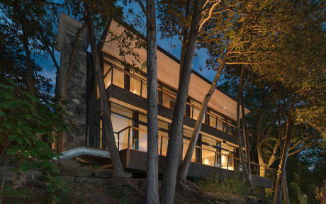 Modern house with lit windows nestled among trees at dusk.