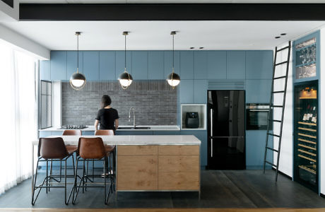 Modern kitchen interior with blue cabinets, bar stools, and a person standing at the