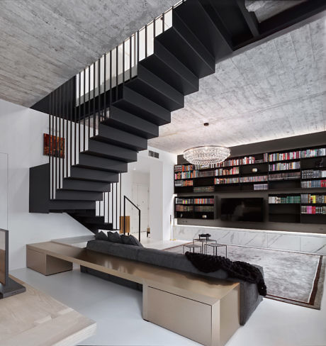 Monochrome living room with floating staircase and full-wall bookshelf.