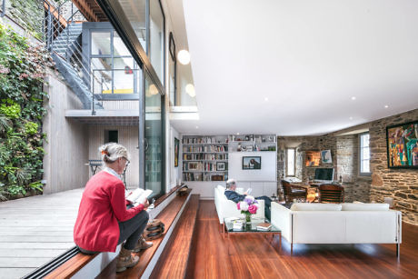 Modern living room with people reading, wooden floors, and large windows.