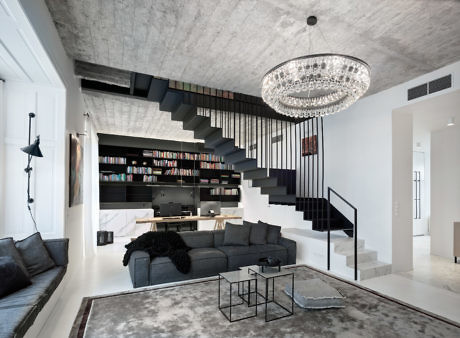 Monochrome living space with exposed concrete ceiling and floating staircase.