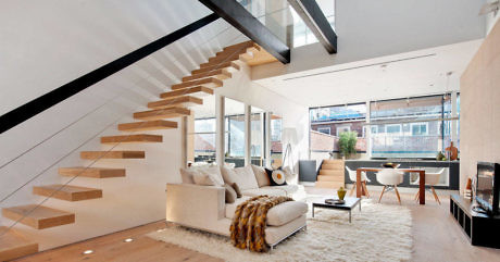 Modern living room with floating staircase and large windows.