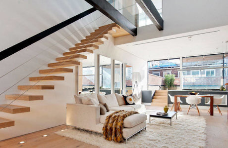 Modern living room with floating staircase and large windows.