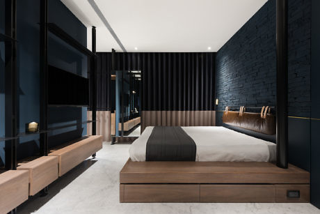 Modern bedroom with dark walls, wooden bed, and sleek furniture.