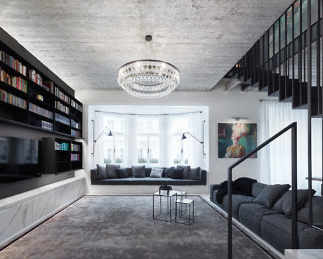 Modern living room with concrete ceiling, large chandelier, and black staircase.